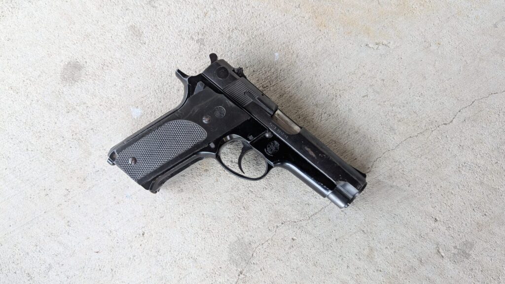 Overhead view of a black Smith & Wesson Model 59 pistol resting on a gray concrete surface.
