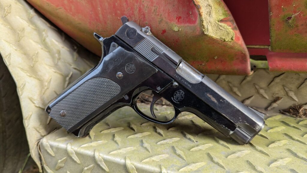 Close-up of the Smith & Wesson Model 59 pistol on a rusty metal diamond plate, clearly showing the "SMITH & WESSON" and "Model 59" roll marks.