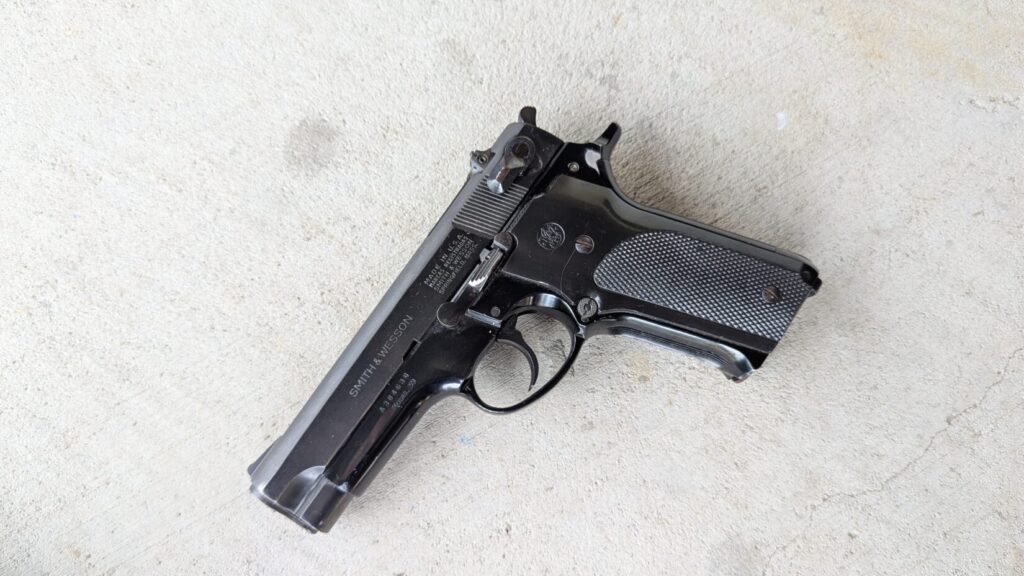 Full-body view of the blued Smith & Wesson Model 59 pistol on a concrete surface, showing the "SMITH & WESSON" marking on the slide.
