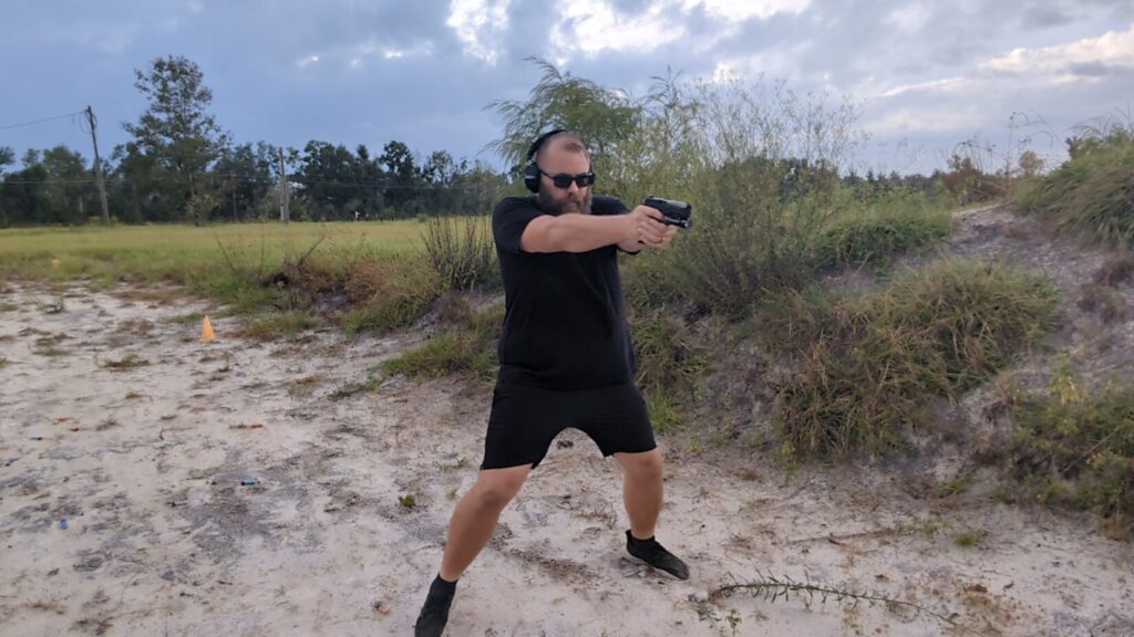 Full-body shot of a man aiming a pistol outdoors while stepping