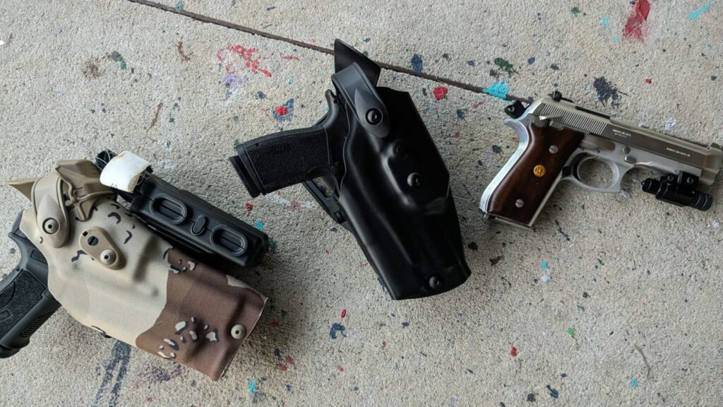 Three handguns and holsters on a colorful concrete surface.