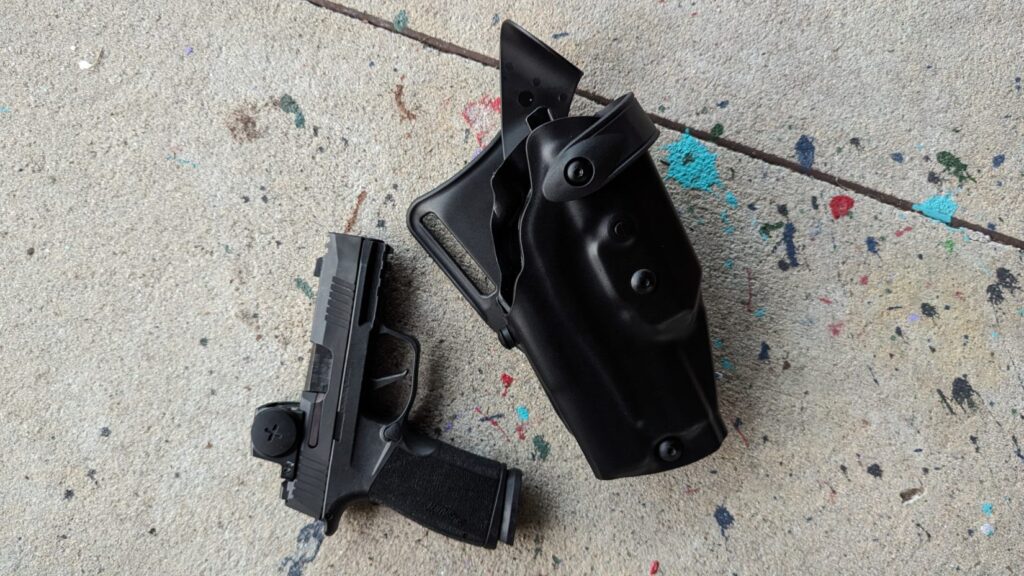 Black handgun with a red dot sight and an empty black holster lying next to it on painted concrete.
