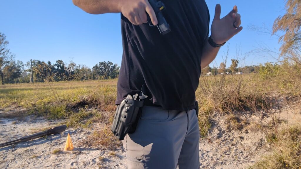 Man drawing a handgun from a black, hip-mounted holster outdoors.