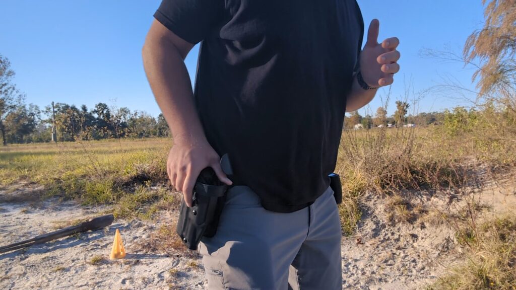 Man drawing a handgun from a black, hip-mounted retention holster outdoors.