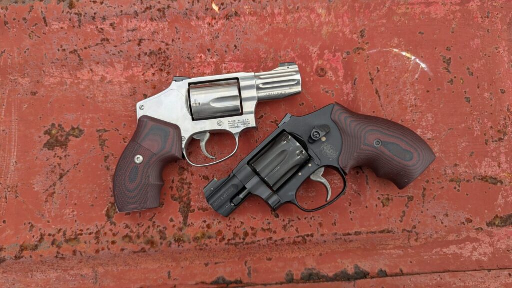 S&W 940 (stainless) and S&W 432 UC (black) snub nose revolvers with custom grips on a rusty red surface.