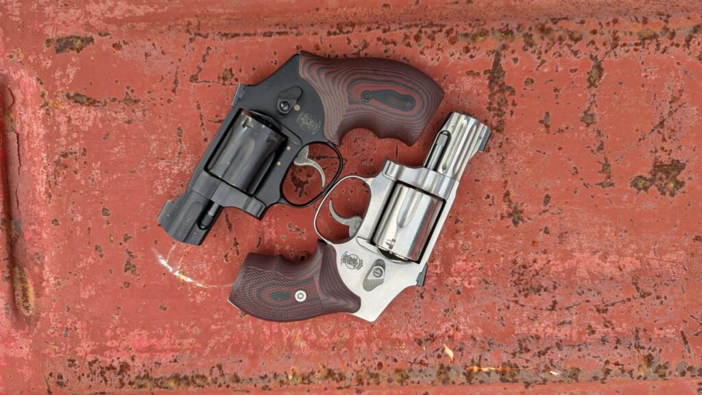 S&W 940 (stainless) and S&W 432 UC (black) snub nose revolvers with custom grips on a rusty red surface.