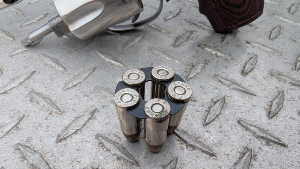 Close-up of a 9mm moon clip fully loaded with five rounds, sitting on a metal diamond plate surface.