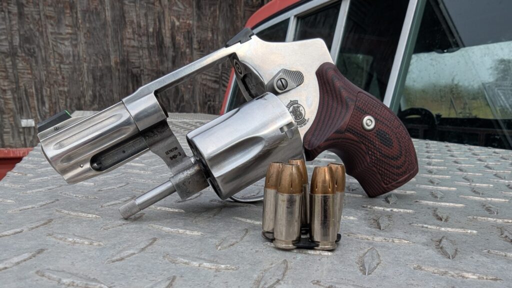 S&W 940 revolver with its cylinder open, alongside a 9mm moon clip loaded with five rounds on diamond plate.