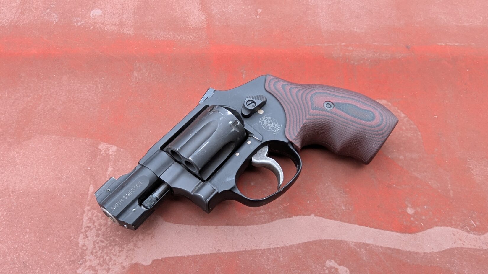 Black S&W 432 UC revolver with a custom grip resting on a rusted red surface.