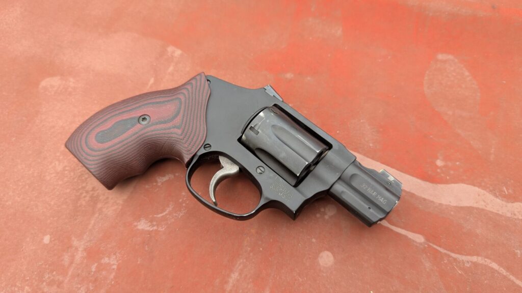 Black S&W 432 UC revolver with a custom grip resting on a rusted red surface.