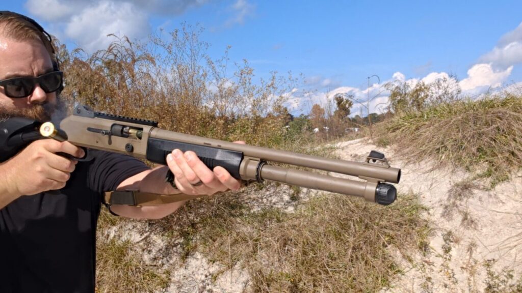 Shooter aiming the Benelli M4 shotgun outdoors.