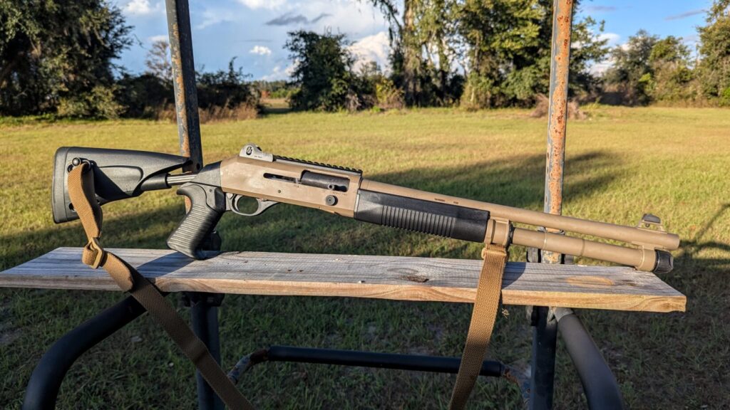 Benelli M4 shotgun with sling resting on a wooden bench in an outdoor range setting.
