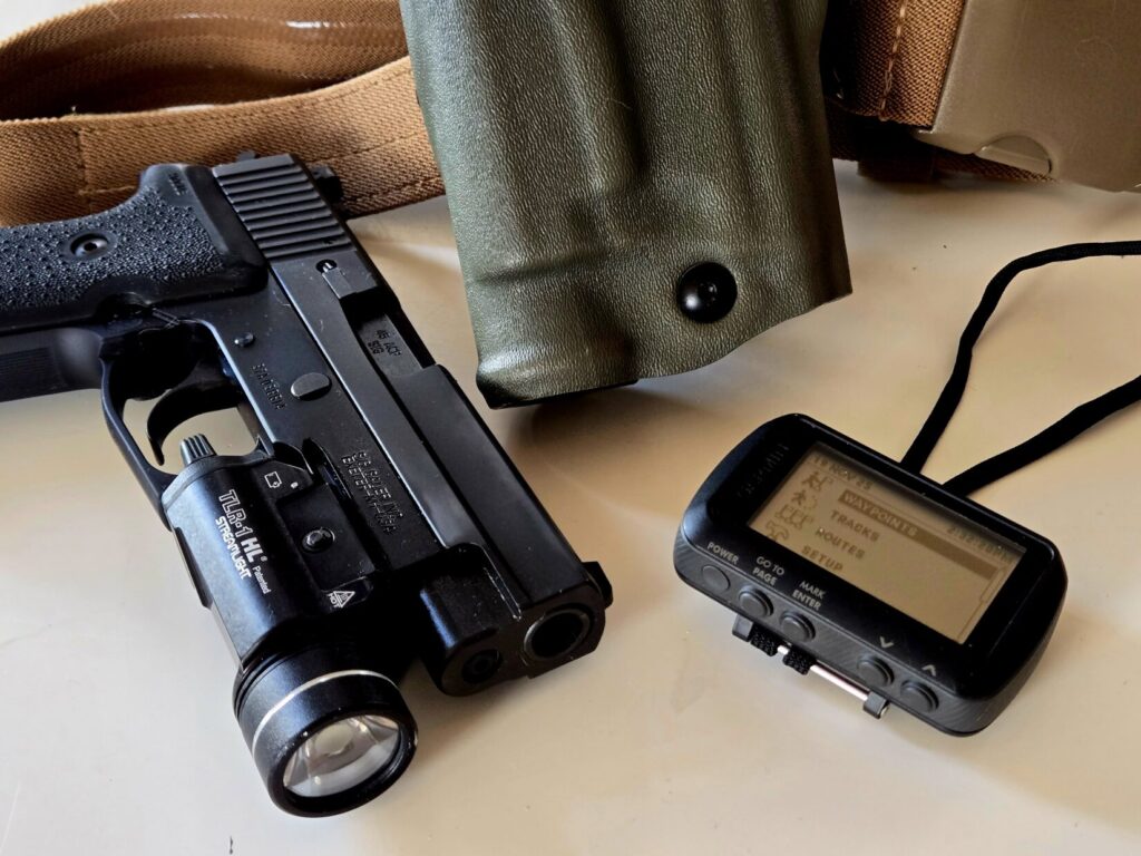 A pistol with weapon light, holster, and GPS unit on a table