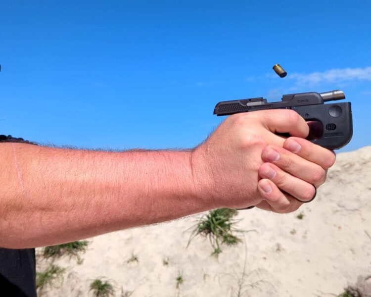 Two-handed grip on handgun during firing, focused shooter.