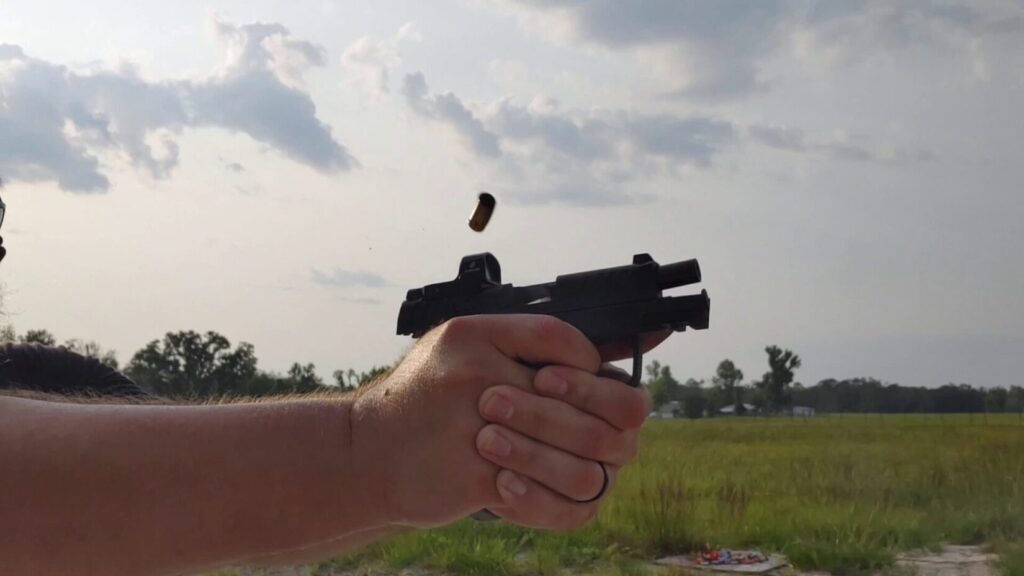 Close-up of strong hand firing pistol with red dot sight, spent casing ejecting.