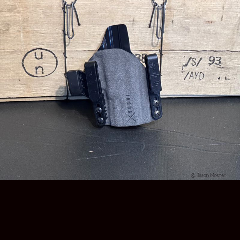 A grey holster with plastic clips on each side, leaning up against a wooden box. 