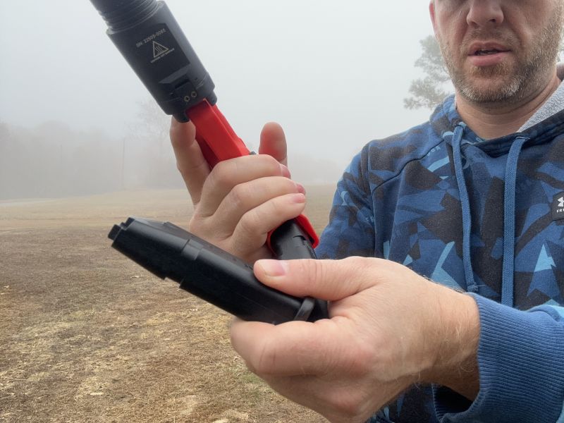 A person in a blue hoodie reloads an orange and black training gun. 