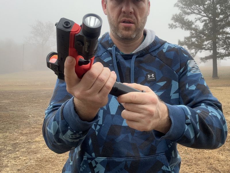 A person in a blue hoodie changing the magazine in an orange and black training gun. 
