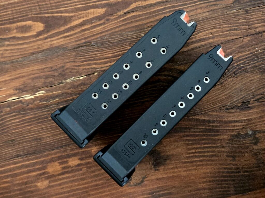 Two Glock pistol magazines with capacities of 15 and 10 rounds on a wooden backdrop.