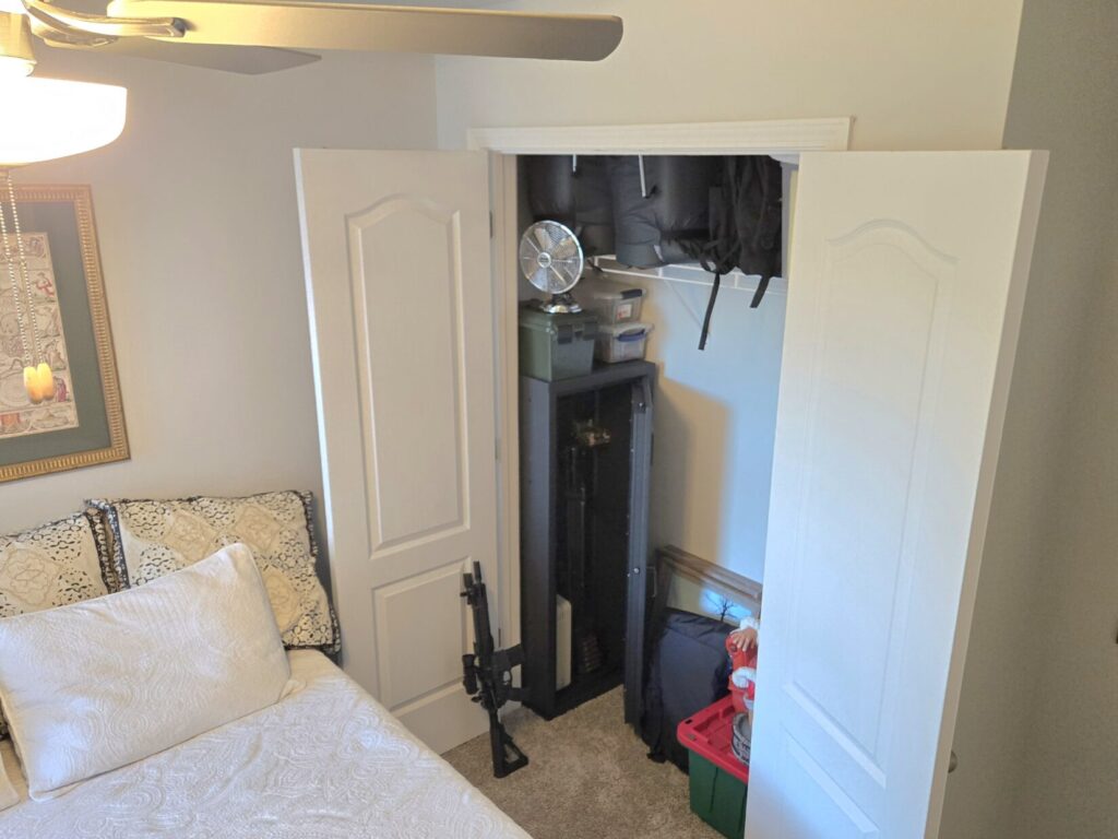 A bedroom closet with a firearms safe and a rifle leaning up against the door