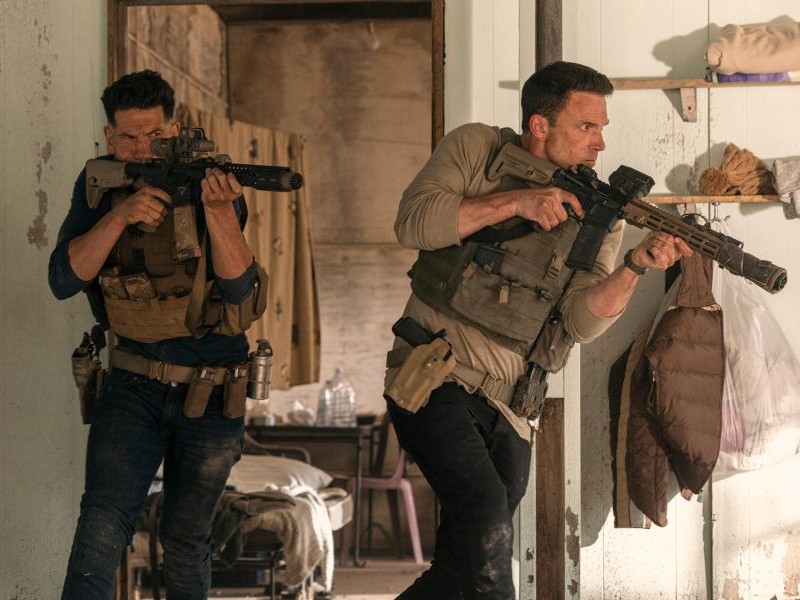 Two men in tactical gear, holding rifles during a gun fight.