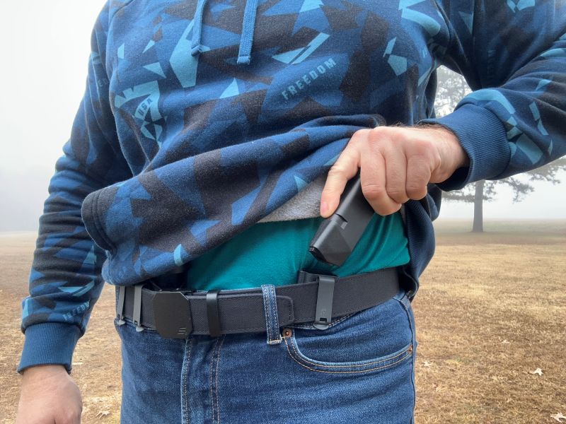 A person in a blue hoodie, drawing a magazine from a concealed magazine pouch. 