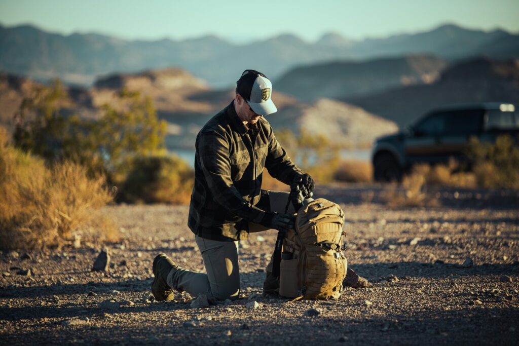 outdoor photo of a man wearing a Vertx Last Line of Defense flannel shirt packing binoculars into a backpack