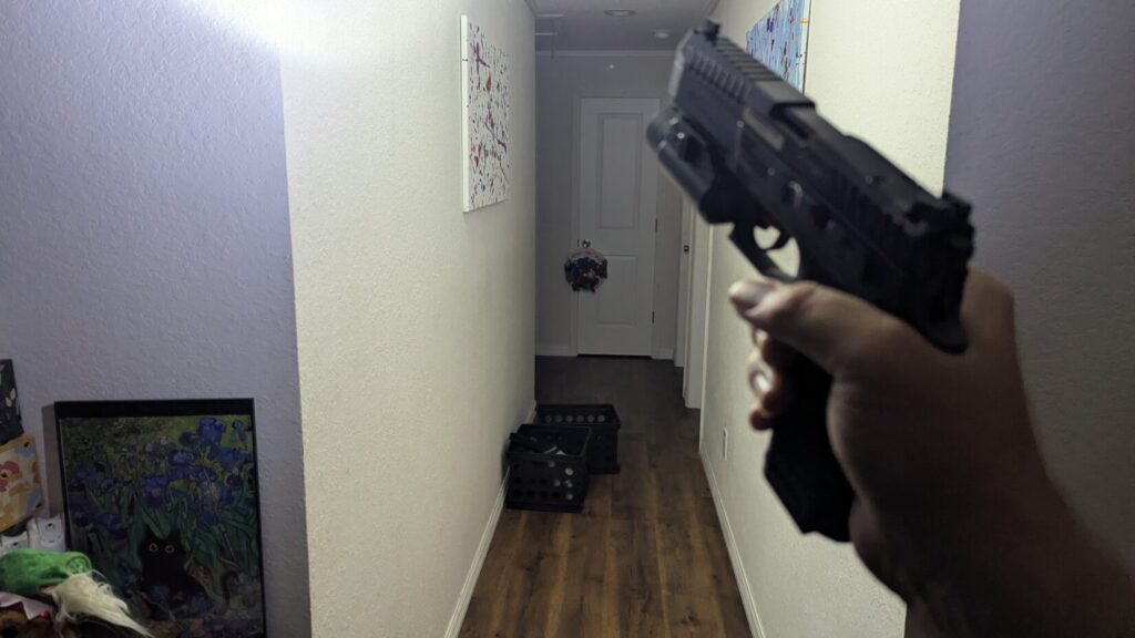 View down a dark hallway, illuminated by the light from a pistol's weapon light.