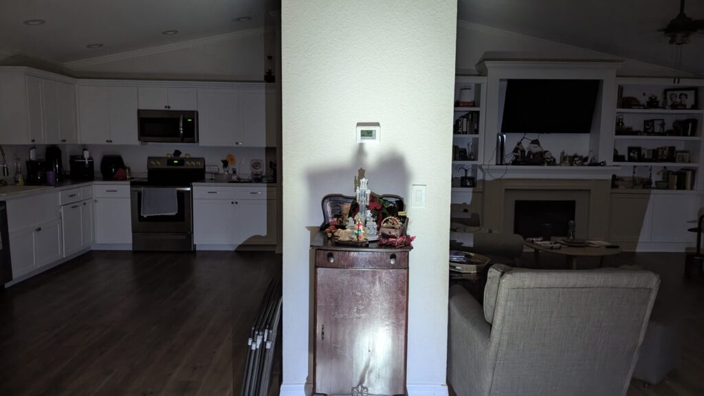 View of a room split by lighting: kitchen and living room dark, center console lit by a flashlight beam.