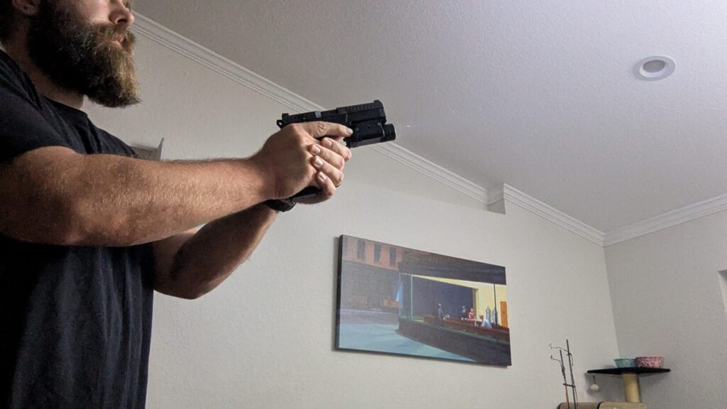 Person aiming pistol with an attached weapon light, creating a bright flare indoors.