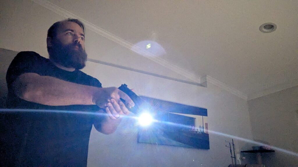 Side view of a person aiming a pistol with an attached weapon light indoors.