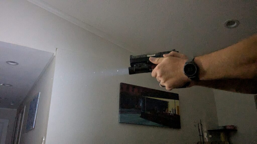 Hands aiming a pistol with an attached weapon light, indoors.