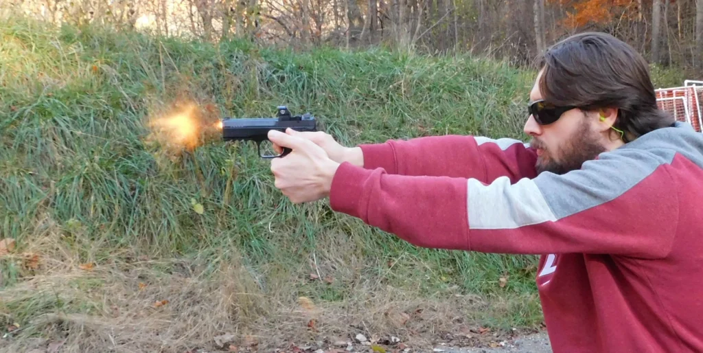 Man firing a semiautomatic pistol with flames coming from the muzzle