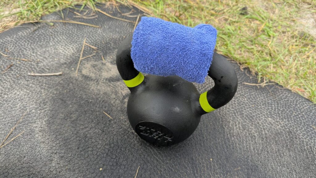 Black kettlebell with a blue towel on the handle, resting on a workout mat. Man firing pump-action shotgun, showing support hand grip on forend.