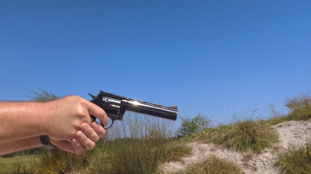 Hands aiming a large-frame, shiny black revolver against a bright blue sky.