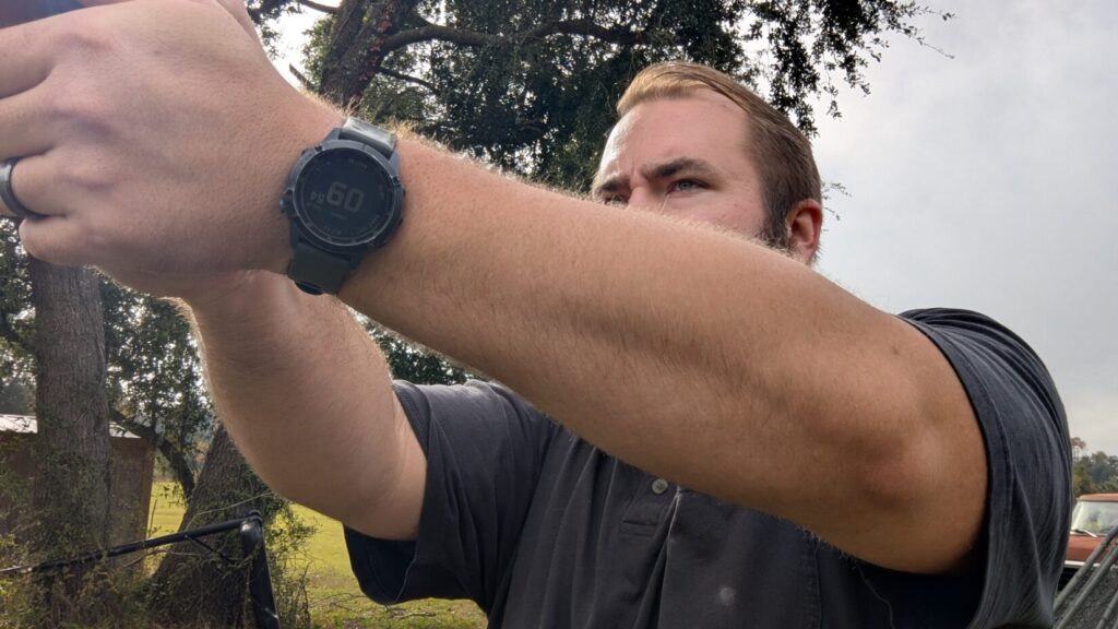 Side profile of a man aiming a pistol, with a focus on his arm and tactical-style wristwatch.
