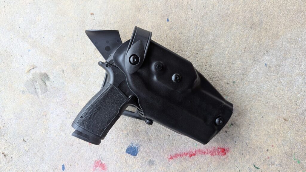 Black Sig Sauer handgun fully holstered in a black retention holster lying on concrete.