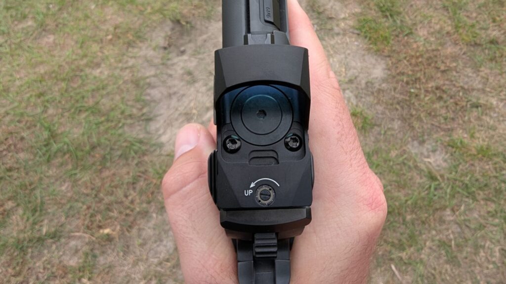 A hand holding a black competition-style pistol with a ported slide and a mounted Cyelee red dot sight over a grassy background.