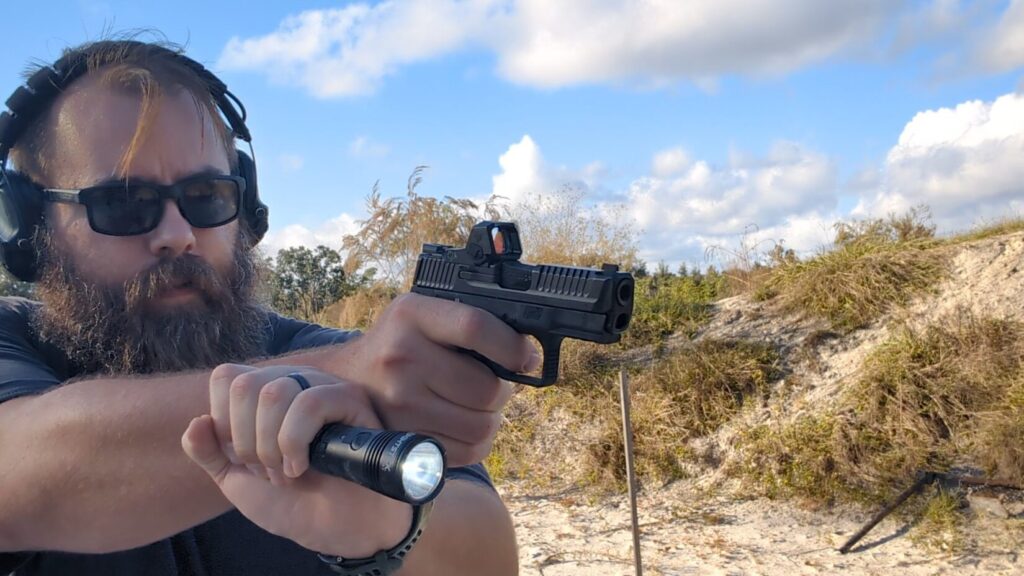 Man shooting pistol outdoors, holding a flashlight in his support hand (Harries technique).