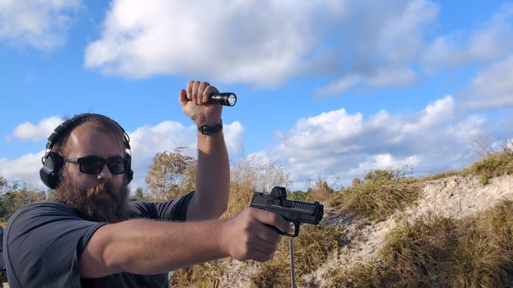 Man shooting pistol outdoors, holding a flashlight overhead FBI Technique