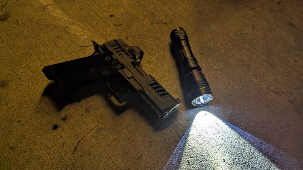 A Staccato pistol and a handheld flashlight with its beam illuminating the concrete floor.