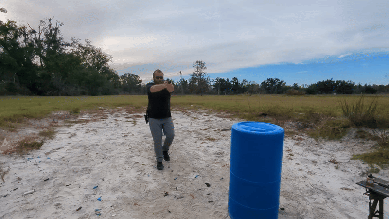 Man moving forward while shooting handgun at an outdoor range.