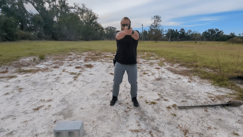 Man shooting handgun in a wide stance, kneeling slightly moving laterally
