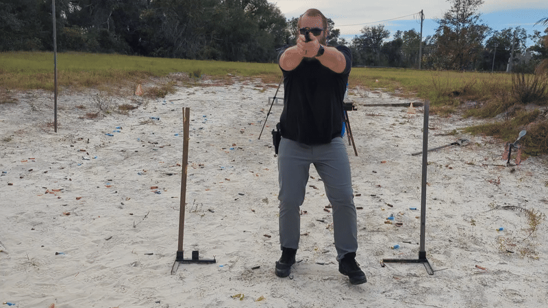 Man drawing and aiming handgun while walking around two poles