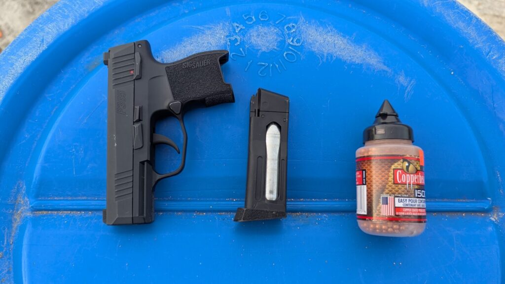 SIG P365 BB pistol on a metal surface next to a magazine and CO2 cartridge