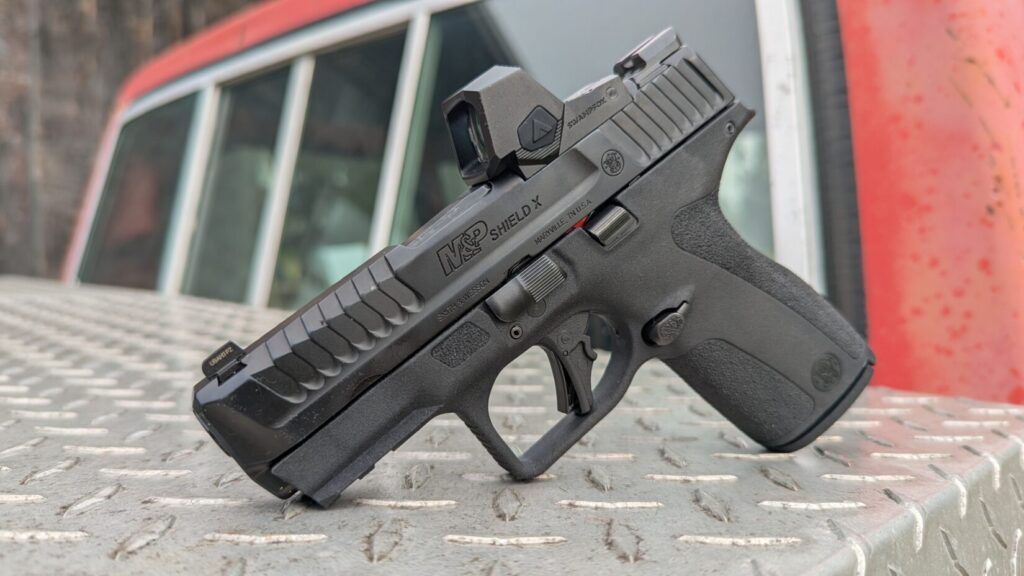 Front view of the M&P Shield X handgun with the red dot optic, showing the muzzle and front slide serrations.