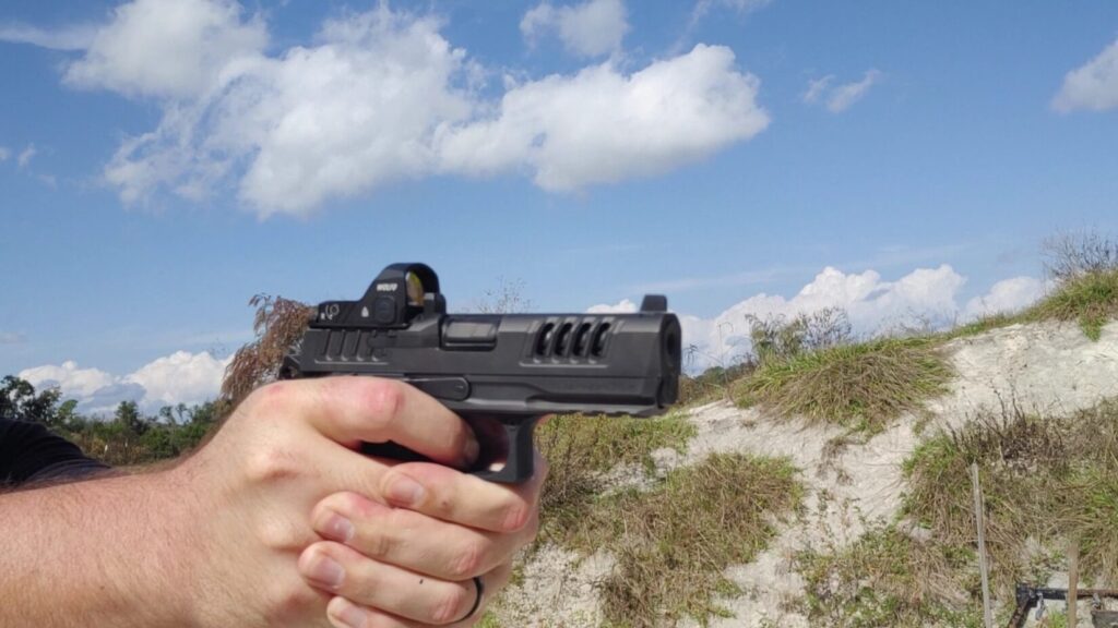Close-up of hands shooting a Staccato HD pistol with slide cuts and a red dot sight