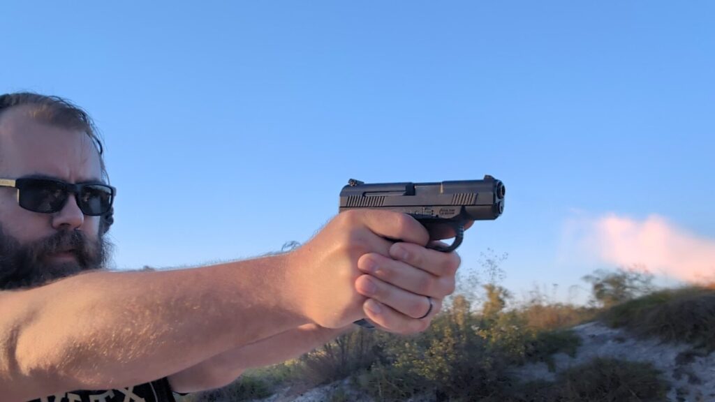 Man with beard and sunglasses aiming the SW99 pistol outdoors.