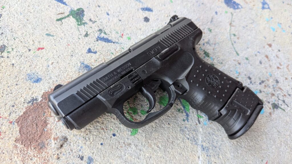 Black compact pistol (SW99) on a concrete floor with paint splatters.