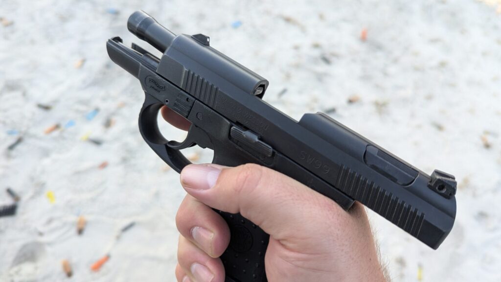 Hand holding a black pistol with the slide locked open